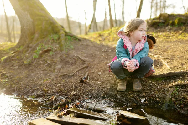 Cute młoda dziewczyna zabawy nad rzeką w ciepły wiosenny dzień. Dziecko bawiące się nad wodą. — Zdjęcie stockowe