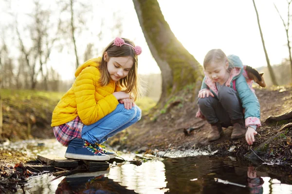 Dos monas hermanas jóvenes divirtiéndose junto a un río en un cálido día de primavera. Niños jugando juntos junto al agua . — Foto de Stock