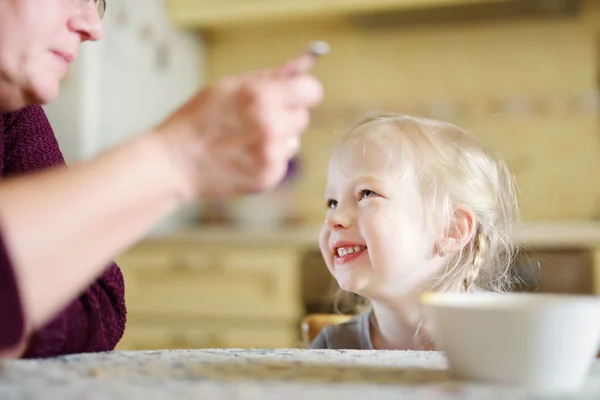 Grandmother feeding her little toddler granddaughter at home. — Stock Photo, Image