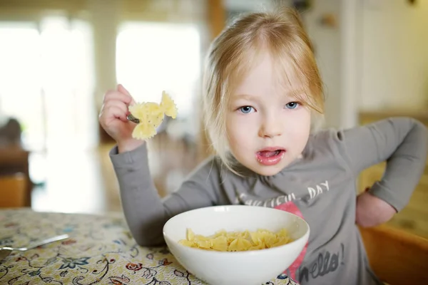 Roztomilé legrační holčička jíst těstoviny nudle doma. — Stock fotografie