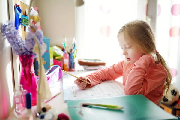 Розумна школярка робить домашнє завдання за своїм столом вдома. Дитина вчиться писати і читати . — стокове фото