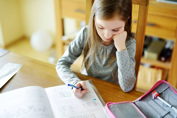 Smart little schoolgirl doing her homework at her table at home. Child learning to write and read. — Stock Photo, Image