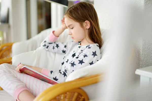Entzückendes Mädchen liest an einem schönen Sommertag ein Buch im weißen Wohnzimmer. Smart schoolgirl macht ihre Hausaufgaben zu Hause nach der Schule. — Stockfoto