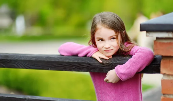 Söt ung flicka står vid ett trästaket på solig sommardag — Stockfoto
