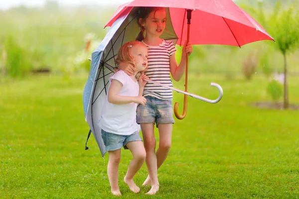 Two cute little sisters holding umbrellas on a rainy summer day — Stock Photo, Image