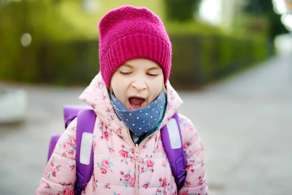 Uma menina adormecida a bocejar a caminho da escola. Criança com uma mochila de manhã . — Fotografia de Stock