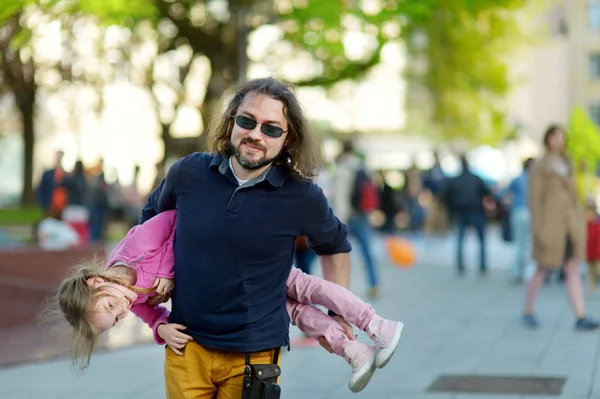 Jonge vader draagt zijn schattige kleine dochter tijdens de zomer stadswandeling. — Stockfoto