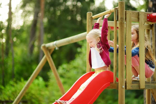 Dwa słodkie dziewczynki, dobra zabawa na placu zabaw na świeżym powietrzu na ciepły, letni dzień — Zdjęcie stockowe