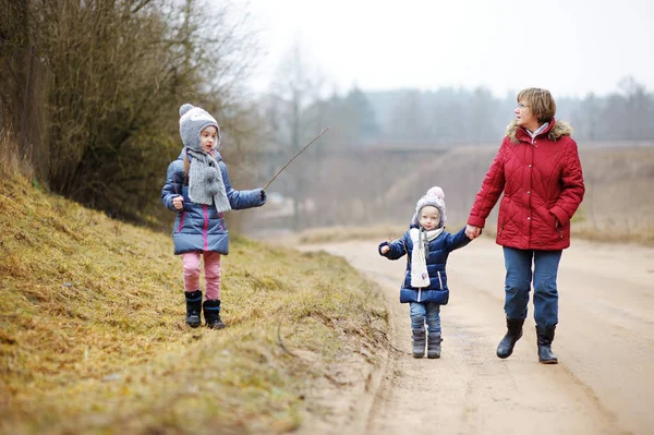 Twee schattige zusjes wandelen in een bos met hun grootmoeder op mooie lentedag. Kinderen die de natuur verkennen. — Stockfoto