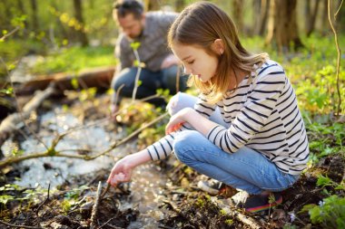 Bahar gününde nehir kenarında eğlenen tatlı bir genç kız. Su kenarında oynayan bir çocuk. Baharın başlarında açık hava aile aktiviteleri.