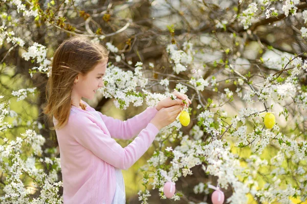 美しい春の日に桜の庭を楽しむ愛らしい少女 桜の枝にイースターエッグをぶら下げている子供 屋外でイースターを祝う子供 — ストック写真