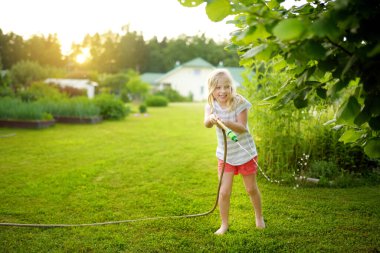 Sıcak bir yaz gününde bahçe hortumuyla oynayan sevimli küçük bir kız. Çocuklar için açık hava yaz aktiviteleri.