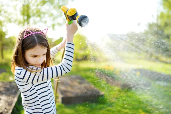 夏天的时候 在花园里给花坛浇水的小女孩很可爱 孩子们在阳光灿烂的日子使用花园软管 妈妈的小助手 — 图库照片