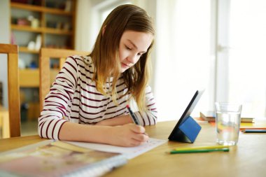 Liseli kız evde dijital tabletle ödevini yapıyor. Çocuk çalışmak için aletler kullanıyor. Çocuklar için eğitim ve uzak mesafe eğitimi. Karantina sırasında evde eğitim. Evde kalıp eğlenin..