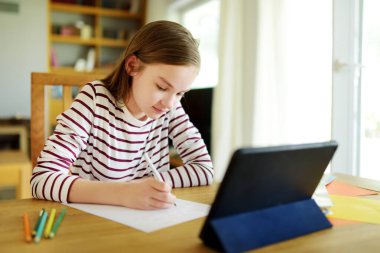 Liseli kız evde dijital tabletle ödevini yapıyor. Çocuk çalışmak için aletler kullanıyor. Çocuklar için eğitim ve uzak mesafe eğitimi. Karantina sırasında evde eğitim. Evde kalıp eğlenin..