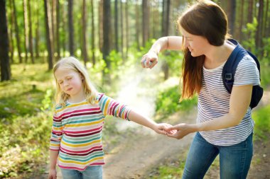 Mother applying insect repellent to her daughter before forest hike beautiful summer day. Protecting children from biting insects at summer. Using bug spray. Active leisure with kids. clipart