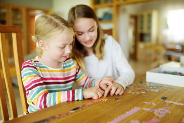 Evde yapboz oynayan sevimli genç kızlar. Çocuklar oturma odasındaki yapboz parçalarını birleştiriyorlar. Çocuklar yapboz yapıyor. Eğlenceli aile eğlencesi. Çocuklar için evde kal..
