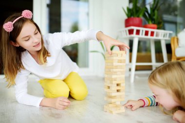 Evde tahta bloklar oyunu oynayan iki kız kardeş. Çocuklar fiziksel ve zihinsel becerilerini geliştiriyorlar. Aile eğlencesi için eğlenceli masa oyunları. Çocuklar için evde kal..