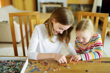Evde yapboz oynayan sevimli genç kızlar. Çocuklar oturma odasındaki yapboz parçalarını birleştiriyorlar. Çocuklar yapboz yapıyor. Eğlenceli aile eğlencesi. Çocuklar için evde kal..