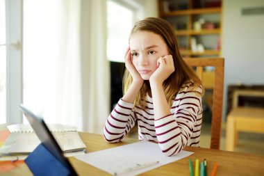 Liseli kız evde dijital tabletle ödevini yapıyor. Çocuk çalışmak için aletler kullanıyor. Çocuklar için eğitim ve uzak mesafe eğitimi. Karantina sırasında evde eğitim. Evde kalıp eğlenin..