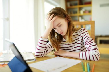 Liseli kız evde dijital tabletle ödevini yapıyor. Çocuk çalışmak için aletler kullanıyor. Çocuklar için eğitim ve uzak mesafe eğitimi. Karantina sırasında evde eğitim. Evde kalıp eğlenin..
