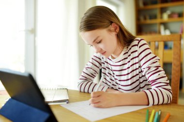 Liseli kız evde dijital tabletle ödevini yapıyor. Çocuk çalışmak için aletler kullanıyor. Çocuklar için eğitim ve uzak mesafe eğitimi. Karantina sırasında evde eğitim. Evde kalıp eğlenin..