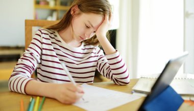 Liseli kız evde dijital tabletle ödevini yapıyor. Çocuk çalışmak için aletler kullanıyor. Çocuklar için eğitim ve uzak mesafe eğitimi. Karantina sırasında evde eğitim. Evde kalıp eğlenin..