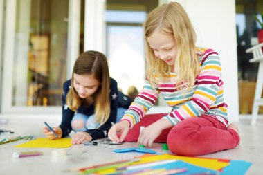 Evde renkli kalemlerle çizim yapan iki genç kız kardeş. Yaratıcı çocuklar birlikte el işi yapıyorlar. Çocuklar için eğitim ve uzak mesafe eğitimi. Karantina sırasında evde eğitim. Evde kalıp eğlenin..