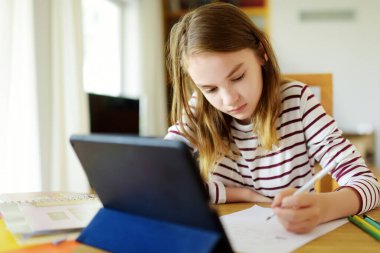 Liseli kız evde dijital tabletle ödevini yapıyor. Çocuk çalışmak için aletler kullanıyor. Çocuklar için eğitim ve uzak mesafe eğitimi. Karantina sırasında evde eğitim. Evde kalıp eğlenin..