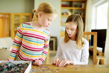 Evde yapboz oynayan sevimli genç kızlar. Çocuklar oturma odasındaki yapboz parçalarını birleştiriyorlar. Çocuklar yapboz yapıyor. Eğlenceli aile eğlencesi. Çocuklar için evde kal..