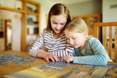 Evde yapboz oynayan sevimli genç kızlar. Çocuklar oturma odasındaki yapboz parçalarını birleştiriyorlar. Çocuklar yapboz yapıyor. Eğlenceli aile eğlencesi. Çocuklar için evde kal..