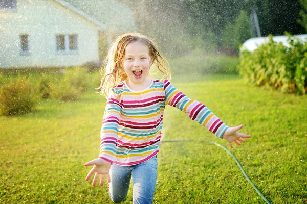 晴れた夏の日に裏庭でスプリンクラーで遊んでいる愛らしい若い女の子 屋外で水を楽しんでいるかわいい子供 子供のための面白い夏のゲーム — ストック写真