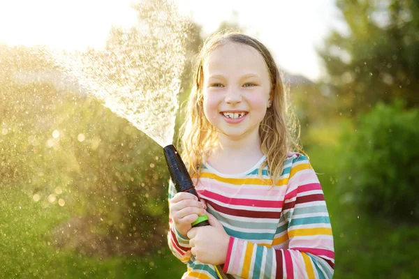 暖かい夏の日に庭のホースで遊ぶ愛らしい少女 暑い日に水遊びをする子供 子供のための屋外夏の活動 — ストック写真