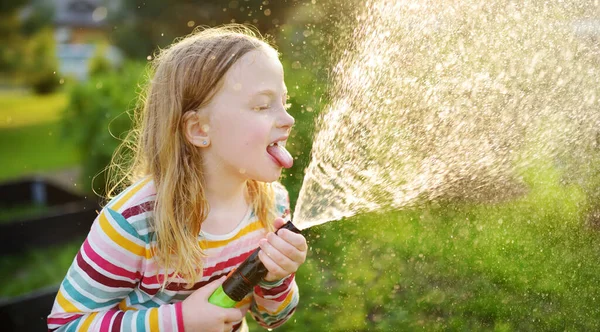 暖かい夏の日に庭のホースで遊ぶ愛らしい少女 暑い日に水遊びをする子供 子供のための屋外夏の活動 — ストック写真