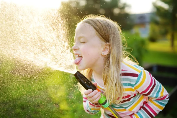 暖かい夏の日に庭のホースで遊ぶ愛らしい少女 暑い日に水遊びをする子供 子供のための屋外夏の活動 — ストック写真