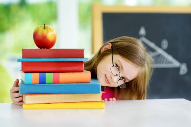 Akıllı liseli kız masasında bir yığın kitapla ders çalışıyor. Genç kız ödevini yapıyor. Çocuklar için eğitim ve uzak mesafe eğitimi. Karantina sırasında evde eğitim. Evde kalıp eğlenin..
