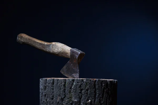 La hache coincée dans la souche de bois sur un fond sombre . — Photo