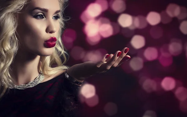 Beautiful blond woman blowing on his hand on background of festive lights. — Stock fotografie