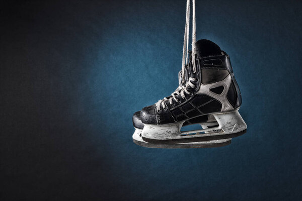 Men's hockey skates hanging on a dark background.
