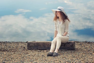 Kızıl saçlı genç kadın rahat sahilde bir yaz gününde oturur..