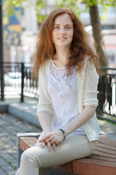 Retrato de uma menina feliz ruiva sentada em um banco no ur — Fotografia de Stock