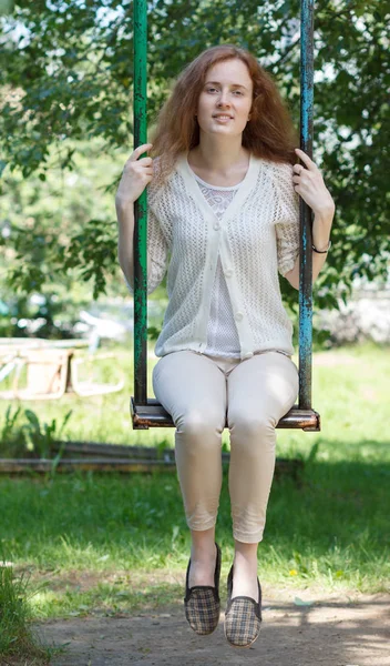 Hermosa joven pelirroja montando en un columpio en un parque de la ciudad . —  Fotos de Stock
