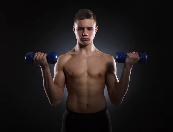 暗い背景にダンベルで筋肉の若い男 — ストック写真