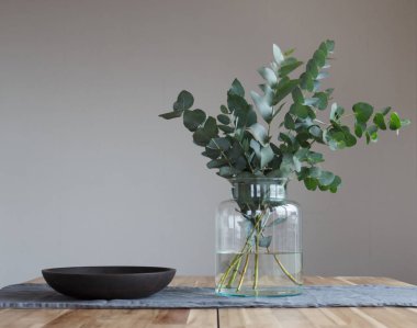 Birkaç dal ve ahşap masa üzerinde bir cam kavanoza yeşil okaliptüs.