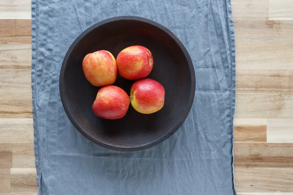 Four red apples in a wooden bowl on a wooden table. The view from the top.