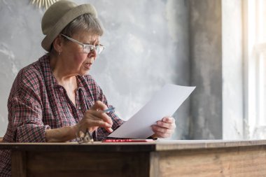 Hesap makinesi ve ödeme belgeleriyle odada bir masada oturan yaşlı bir kadın..