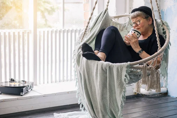 Een Oudere Vrouw Met Een Beker Haar Handen Luisterend Naar — Stockfoto