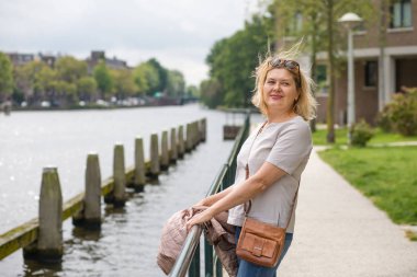 Mutlu yaşlı bir kadın, şehir kanalında ayakta durarak bir yaz gününün tadını çıkarıyor. Yaşlıların aktif yaşam tarzı kavramı.