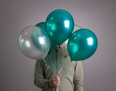 Adam yüzünü bir balon yığınının arkasına saklar..