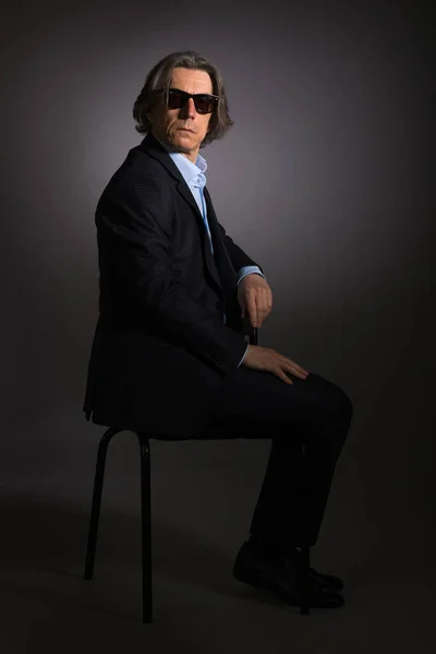 Homem Óculos Sol Terno Elegante Preto Está Sentado Uma Cadeira — Fotografia de Stock